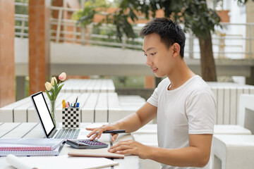 Online studying concept a male student in white t-shirt studying online by using his new white laptop and the calculator in the accounting class