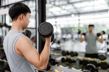 Fototapeta na wymiar exercise concept The male sport member lift black dumbbells up with both hands, standing and doing concentration curl posture while looking at the mirror