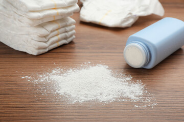 Bottle, scattered dusting powder and diapers on wooden background. Baby care products