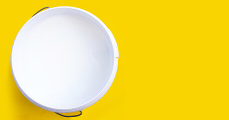 White paint in plastic bucket on yellow background.