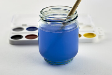 watercolor paints and a paint brush in a jar of water on a white background