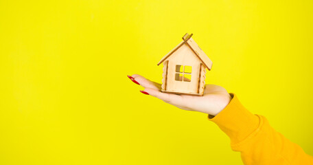 Fototapeta na wymiar Young woman's hand with small wooden house. Crop unrecognizable person holding small toy house. Concept of purchasing new apartment and roof overhead.