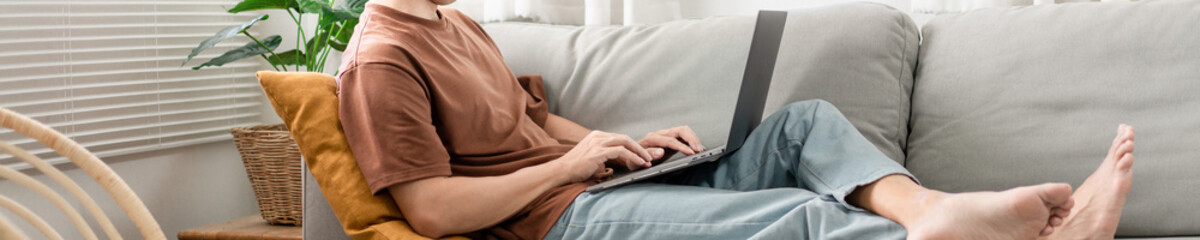 Technology Concept The man that is putting on glasses leaning his back on the dark yellow while focusing on the laptop&rsquo;s screen