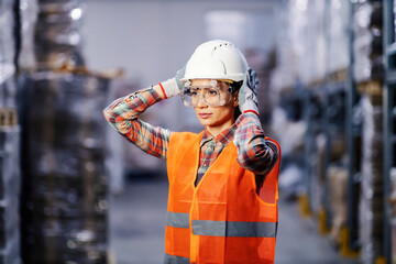 Portrait of female storage worker putting protective mask and helmet and preparing for hard work in...