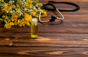 Herbal oil in a glass bottle. Cosmetic organic essential oil. Bunch of healing herbs on wooden table. Herbal medicine bottle with flowers. Fresh herbs from the garden for aromatherapy.