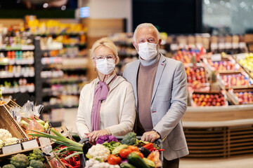 Happy senior couple shopping organic vegetables at supermarket during corona virus.