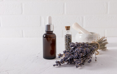 serum with an extract of lavender herbs for face and body skin care in a glassbottle on a white table and the brick wall.