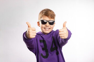 Studio shot of appy smiling boy in sunglasses showing thumb up isolated on white background.