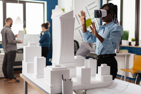 Architect Using Vr Headest To Look At White Foam Scale Model Of Real Estate Project. Engineer Working With Augmented Reality Looking At Table With Skyscraper Building Maquette.