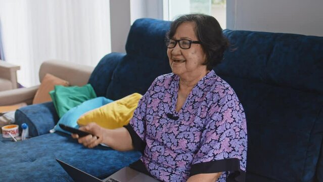 Asian Senior Woman Laughing And Watching Tv In Sofa At Home