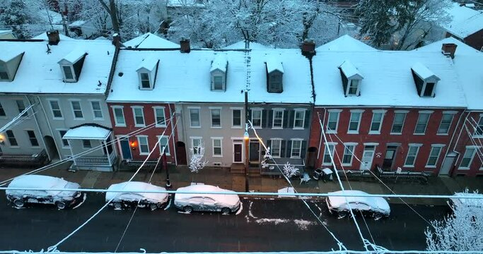 Person walks dog on city sidewalk. Rowhomes in winter snow at night. Flurries in aerial truck shot.