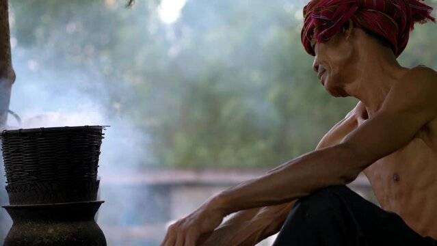 Close up, Senior man shirtless and turban in loincloth steamed sticky rice with a wood stove according of life of the rural people, The simple life in Thailand