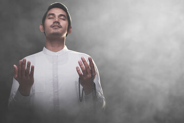 Asian Muslim man standing while raised hands and praying