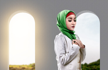 Asian Muslim woman in a veil standing while raised hands and praying