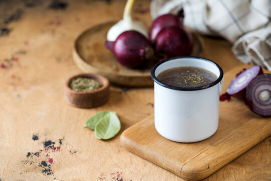 Homemade healthy bone broth with spices in a white mug on a wooden board.