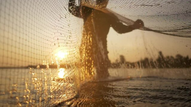 Slow motion shot, Silhouette Asian Senior Fisherman wearing eyeglasses standing in water and fishing net to fishing at river in early morning