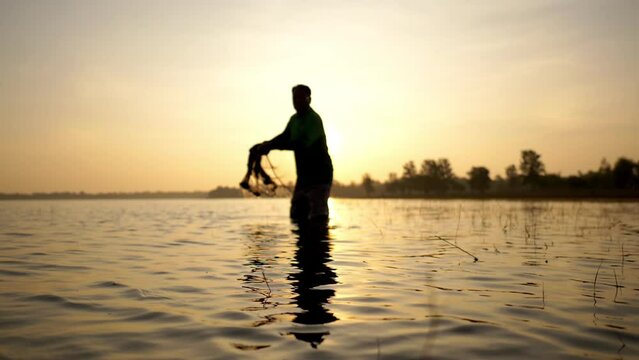 Slow motion shot, Silhouette Asian Senior Fisherman wearing eyeglasses standing in water and fishing net to fishing at river in early morning