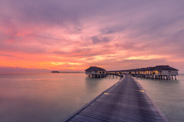 Fototapeta na wymiar Fantastic sunset landscape in the Maldives. Amazing clouds and colorful sky water villas, bungalows over tranquil ocean lagoon. Tropical island beach, sea, traveling destination. Luxury vacation