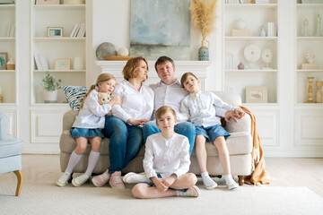 Portrait large family spending time together at home. They are happily sitting in the living room on the couch in a modern light interior. Caucasian parents with children spend time on weekends