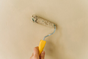 the hand holds a paint roller and paints the wall close-up. paint the wall beige. roller smeared in beige paint