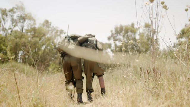 Injured soldiers supporting his team mate and limping over a dry vegetation to the habited world. Dramatic following shot