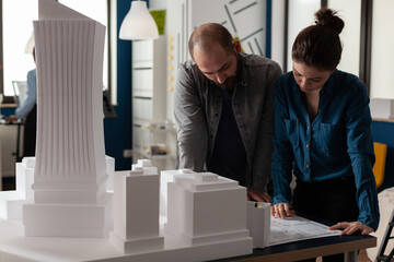 Team of two architects colleagues collaborating looking down at blueprints of urban planning project. Architectural engineers doing teamwork reading construction plans.