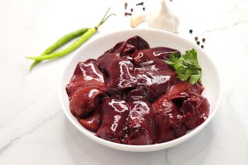 Raw chicken liver in a white plate along with spices such as garlic, black pepper, green chili, and coriander. Kaleji. Copy space.