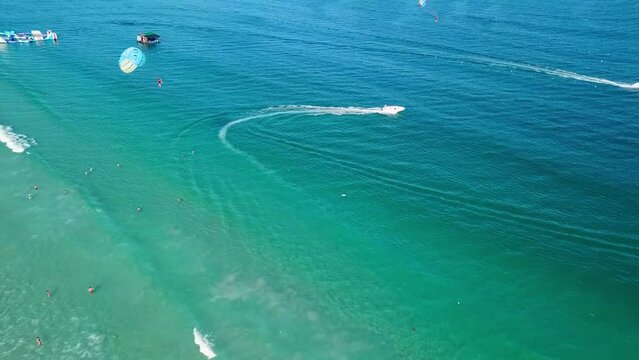 Tourists parasailing over sea coastline, drone point view. Aerial footage of people on parachute above tropical beach.