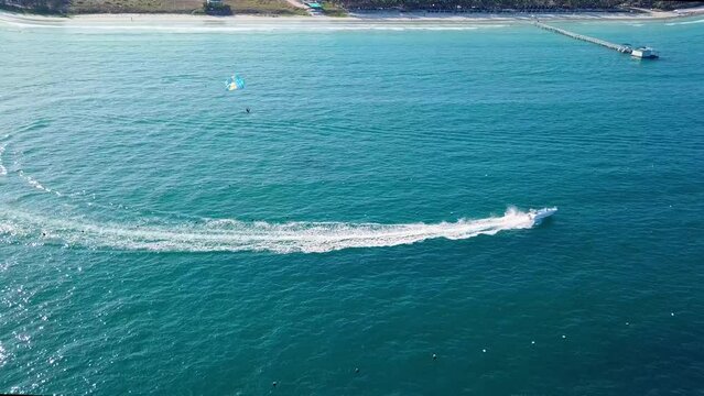 Tourists parasailing over sea coastline, drone point view. Aerial footage of people on parachute above tropical beach.