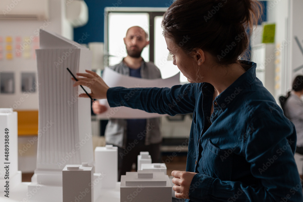 Poster architect inspecting futuristic building design of skyscraper with colleague engineer holding bluepr