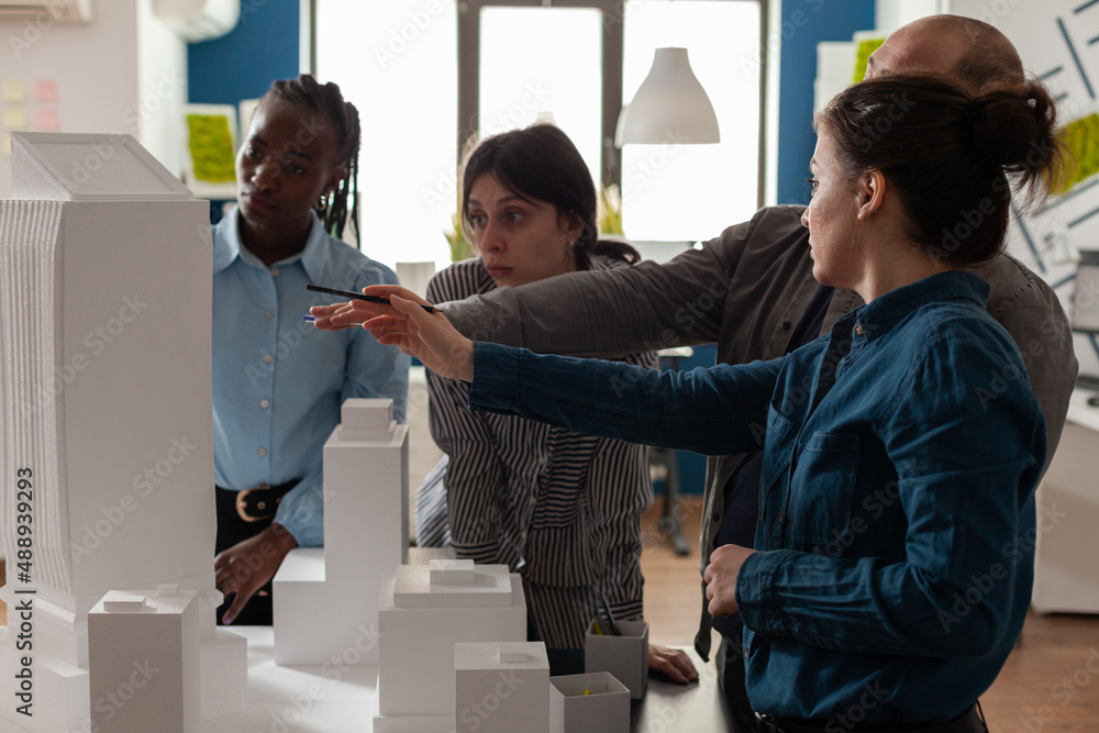Poster team of professional architects brainstorming ideeas pointing at real estate construction model in a