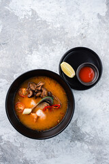 Traditional spicy Thai soup Tom Yum with shrimp and seafood in ceramic bowl on stone background