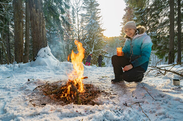 A woman at a campfire in winter in the forest drinks tea from a glass. - 488940406