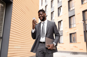 Smiling african american businessman chatting with client on smartphone, having break and walking outdoors