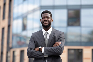 Fototapeta premium Wealthy african american entrepreneur young man standing outside modern office building, posing with folded arms