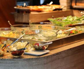 fermented olive, garlic, lettuce and fruits in glass bowls on ice and caprese salad on white plate with stainless steel tongs at hotel cold buffet