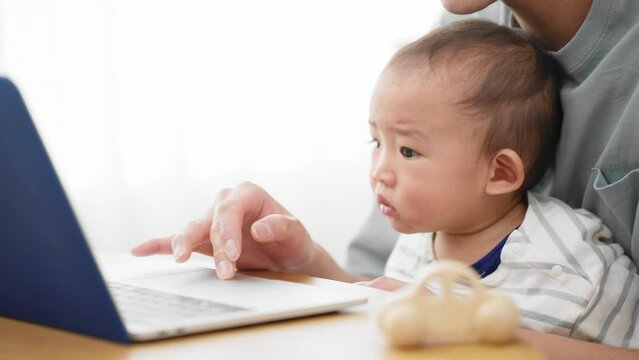 ノートパソコンを赤ちゃんに見せる父親