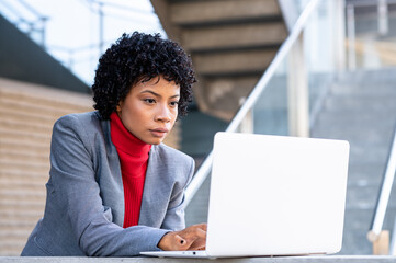 Obraz na płótnie Canvas Una elegante mujer afroamericana trabajando con su ordenador portátil en un edificio de oficinas