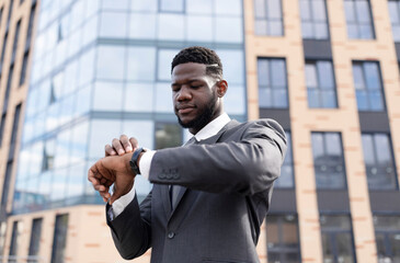 Fototapeta premium Time management. Focused african american businessman looking at wristwatch, walking during break in downtown area