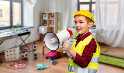 building, construction and profession concept - little boy in protective helmet and safety vest talking to megaphone over children's room at home background