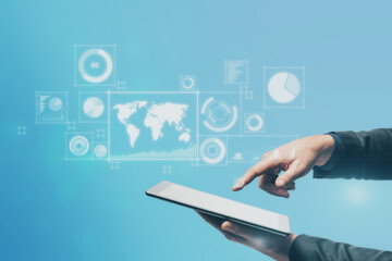 Close up of businessman hand pointing at tablet with abstract digital business interface on blurry blue background. Technology, finance, success, economy and growth concept. Double exposure.