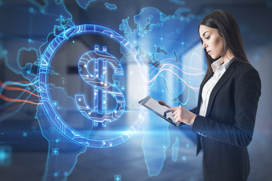 Attractive young european business woman using tablet with abstract glowing blue dollar sign and map with charts on blurry office interior background. 