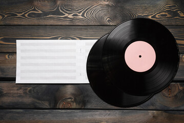 Blank note music book with copy space and vinyl records on the wooden table flat lay background.