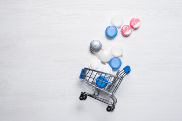 Contact lenses container in the shopping cart on the white wooden flat lay background with copy...