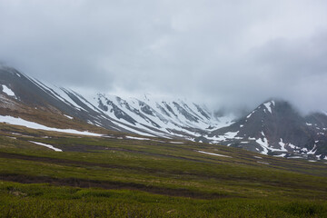 Dramatic alpine landscape with snowy mountains in gray low clouds. Bleak atmospheric scenery of...