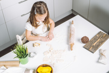 Obraz premium Portrait of little serious girl, helping, making shape dough easter cookies. Sculpt dough flour bakery cup biscuit. Preparing rolling pin. Wood plate of yellow eggs, plant. Kitchen utensil indoor.