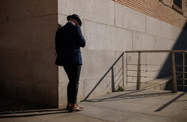 Full length of adult man in hat and suit talking on phone on street against wall. Madrid, Spain