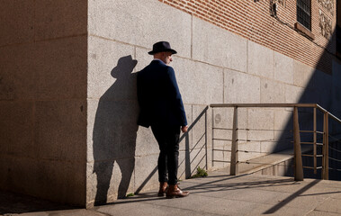 Full length of adult man in hat and suit standing on street against wall. Madrid, Spain