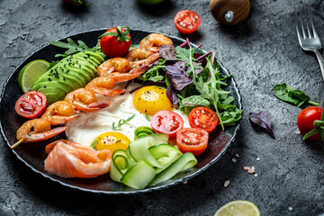 Ketogenic breakfast. Keto low carb salmon, grilled shrimps, prawns, fried eggs, fresh salad, tomatoes, cucumbers and avocado. keto diet. Top view