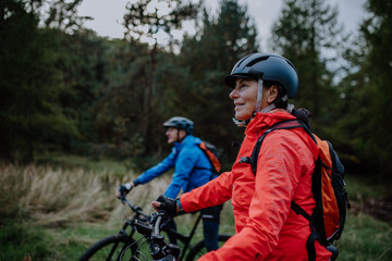 Senior couple bikers with e-bikes admiring nature outdoors in forest in autumn day.